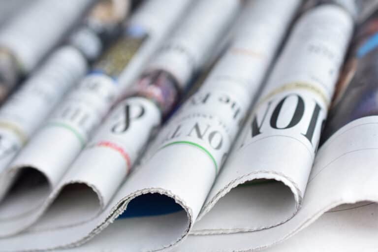 OpenAI utilizes news outlets' articles for ChatGPT training without permission or payment, while newspapers stack on a white surface remain unnoticed.